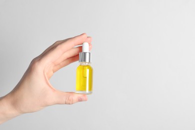 Photo of Woman holding bottle of cosmetic oil on light background, closeup. Space for text