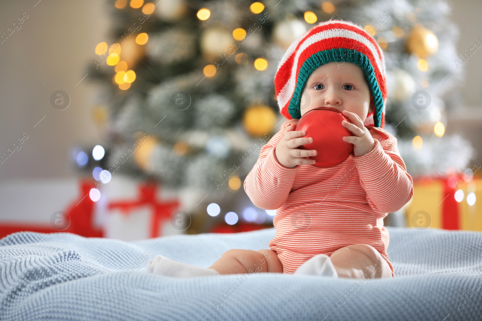 Photo of Little baby wearing elf hat on blanket indoors. First Christmas