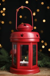 Christmas lantern with burning candle and decor on wooden table against blurred festive lights. Greeting card design
