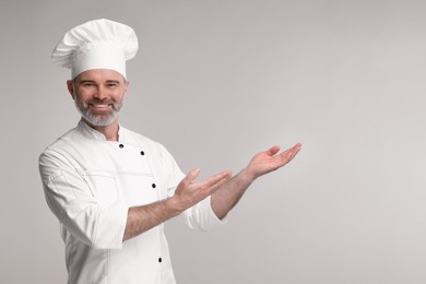 Happy chef in uniform showing something on grey background, space for text