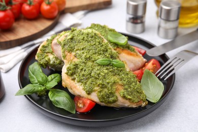 Delicious chicken breasts with pesto sauce, tomatoes and cutlery served on light table, closeup