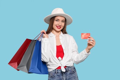 Photo of Stylish young woman with shopping bags and credit card on light blue background
