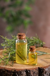 Bottles of essential oil and fresh tarragon leaves on wooden stump. Space for text