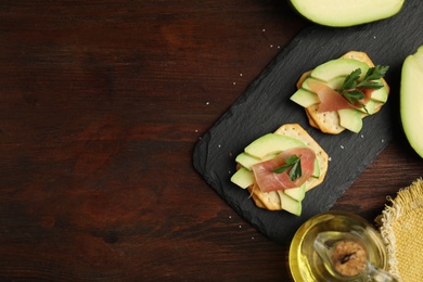 Photo of Delicious crackers with avocado, prosciutto and parsley on wooden table, flat lay. Space for text