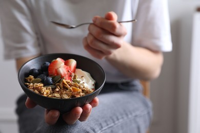 Photo of Woman eating tasty granola with berries, yogurt and seeds indoors, closeup