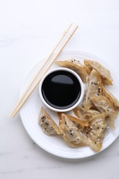 Delicious gyoza (asian dumplings), soy sauce and chopsticks on white table, top view