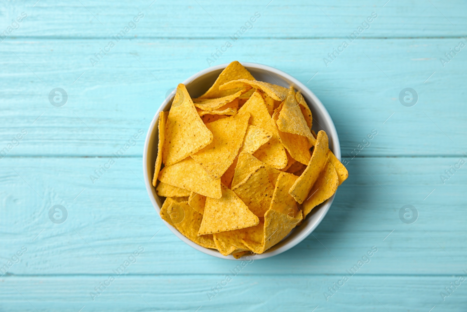 Photo of Tasty mexican nachos chips in bowl on blue wooden table, top view