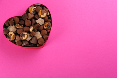 Different delicious chocolate candies in heart shaped box on pink background, top view. Space for text