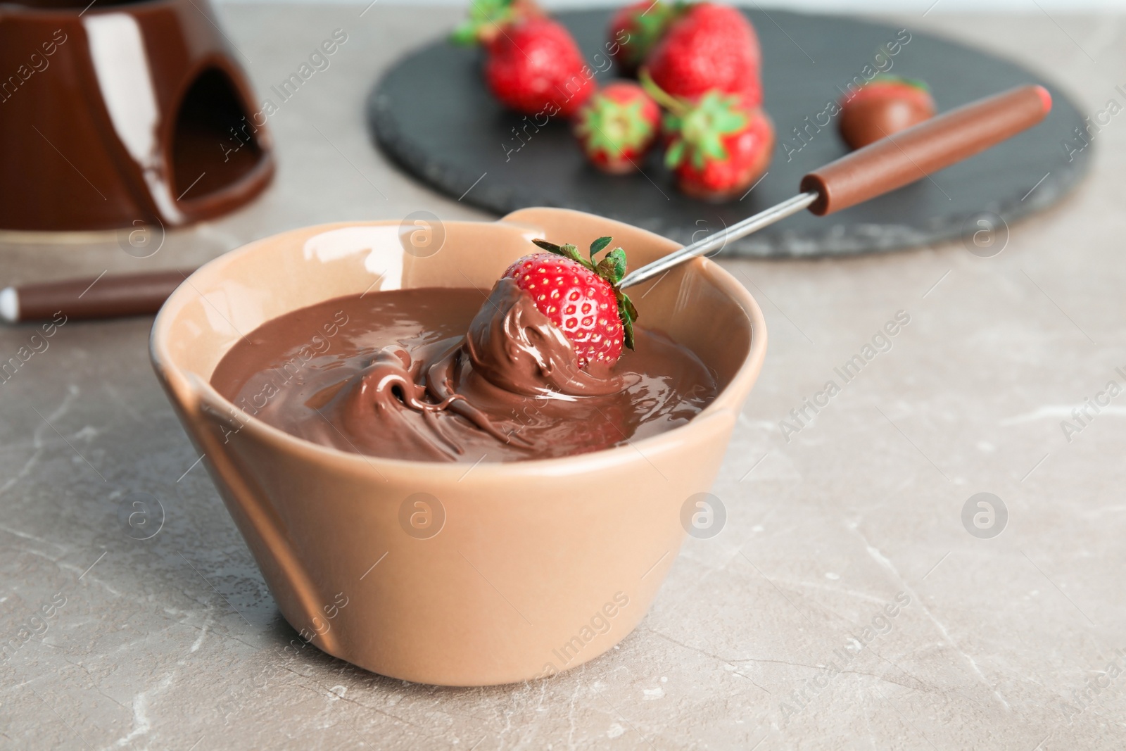 Photo of Ripe strawberry dipped into chocolate fondue on table