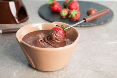 Ripe strawberry dipped into chocolate fondue on table