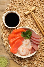 Photo of Delicious sashimi set of salmon, shrimps and tuna served with funchosa, parsley, wasabi and soy sauce on wooden table, flat lay
