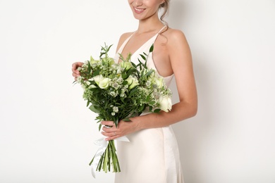 Photo of Young bride wearing wedding dress with beautiful bouquet on light background, closeup