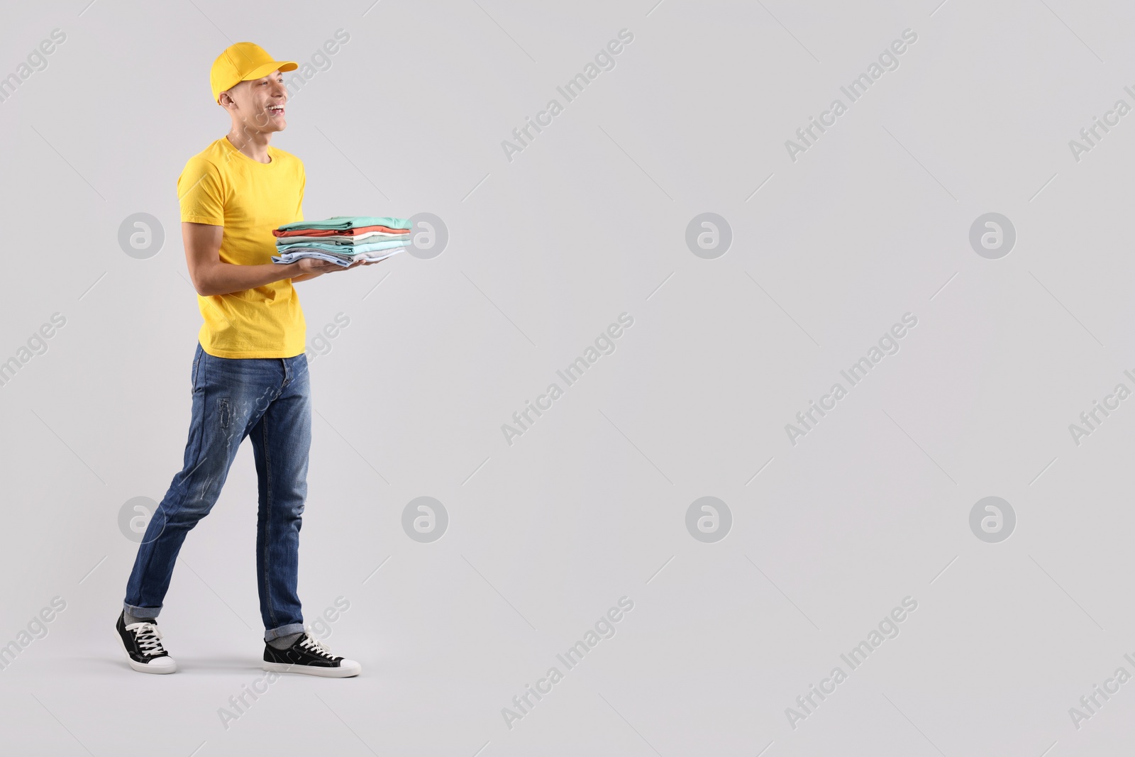 Photo of Dry-cleaning delivery. Happy courier holding folded clothes on light grey background, space for text