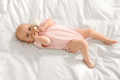 Photo of Cute little baby with toy on white sheets, top view