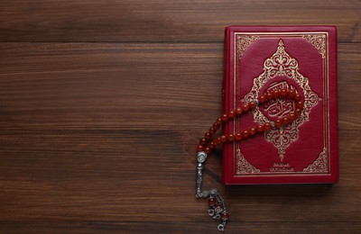 Photo of Muslim prayer beads and Quran on wooden table, top view. Space for text