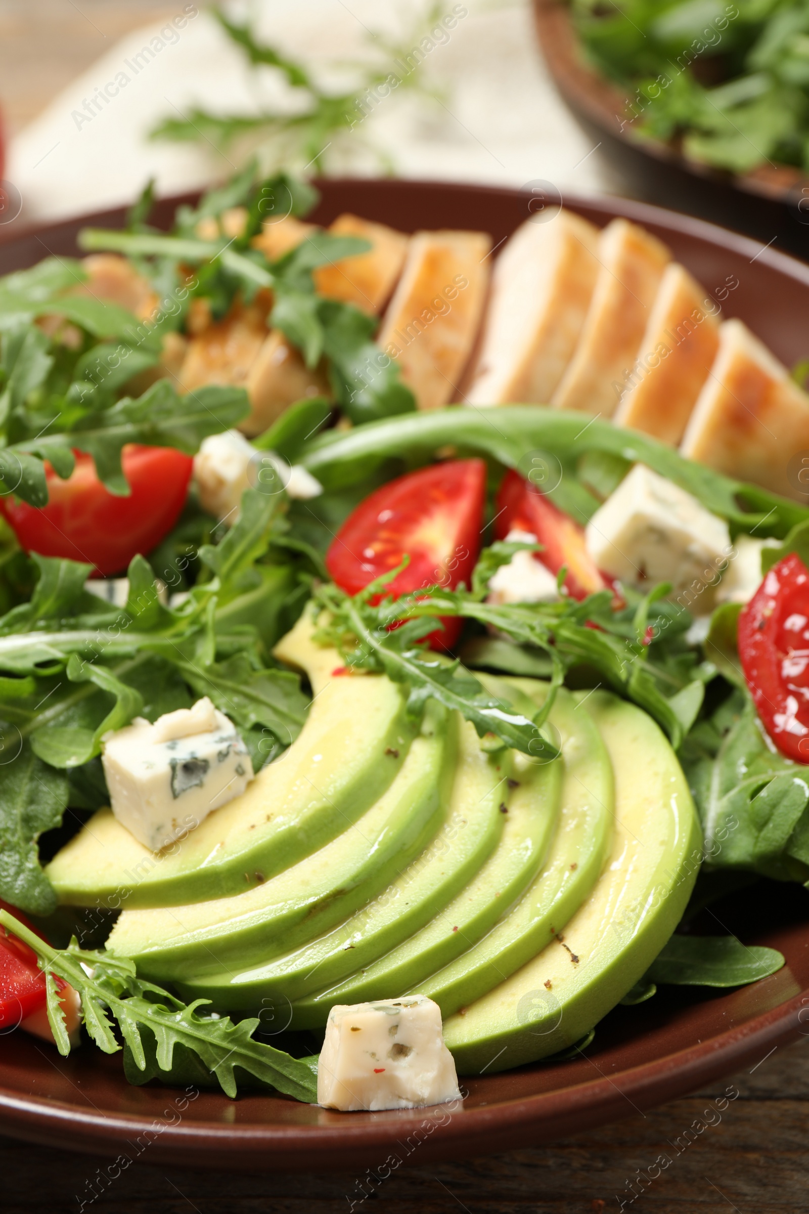 Photo of Delicious salad with chicken, arugula and avocado in bowl, closeup