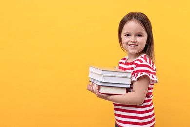 Photo of Cute little girl with books against orange background. Space for text