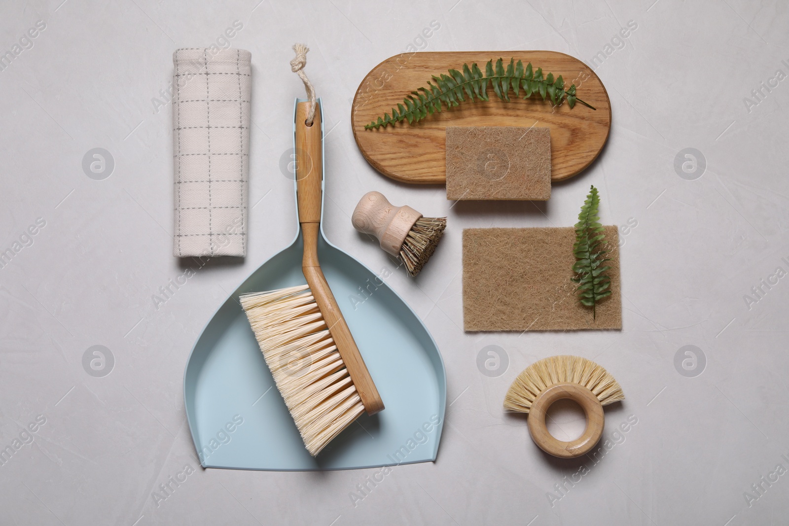 Photo of Cleaning brushes, scoop, sponges, towel and fern leaves on light grey background, flat lay