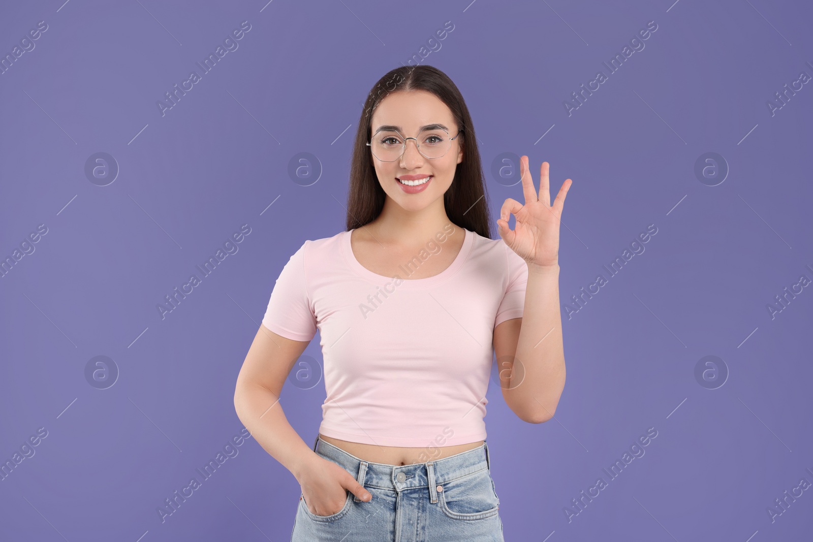 Photo of Beautiful woman in glasses showing OK gesture on violet background