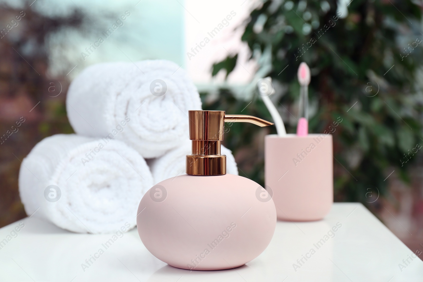 Photo of Soap dispenser and bathroom essentials on table against blurred background