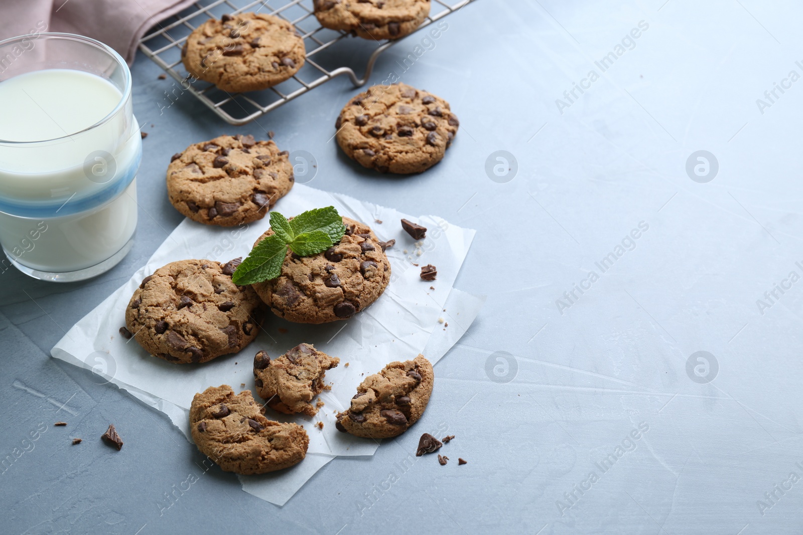 Photo of Tasty chocolate chip cookies, glass of milk and mint leaves on light grey table. Space for text