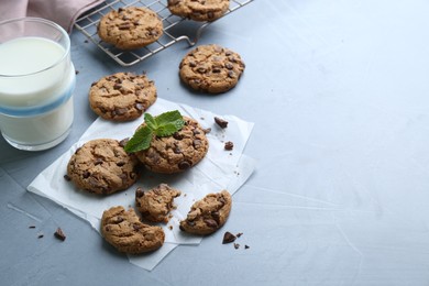 Photo of Tasty chocolate chip cookies, glass of milk and mint leaves on light grey table. Space for text