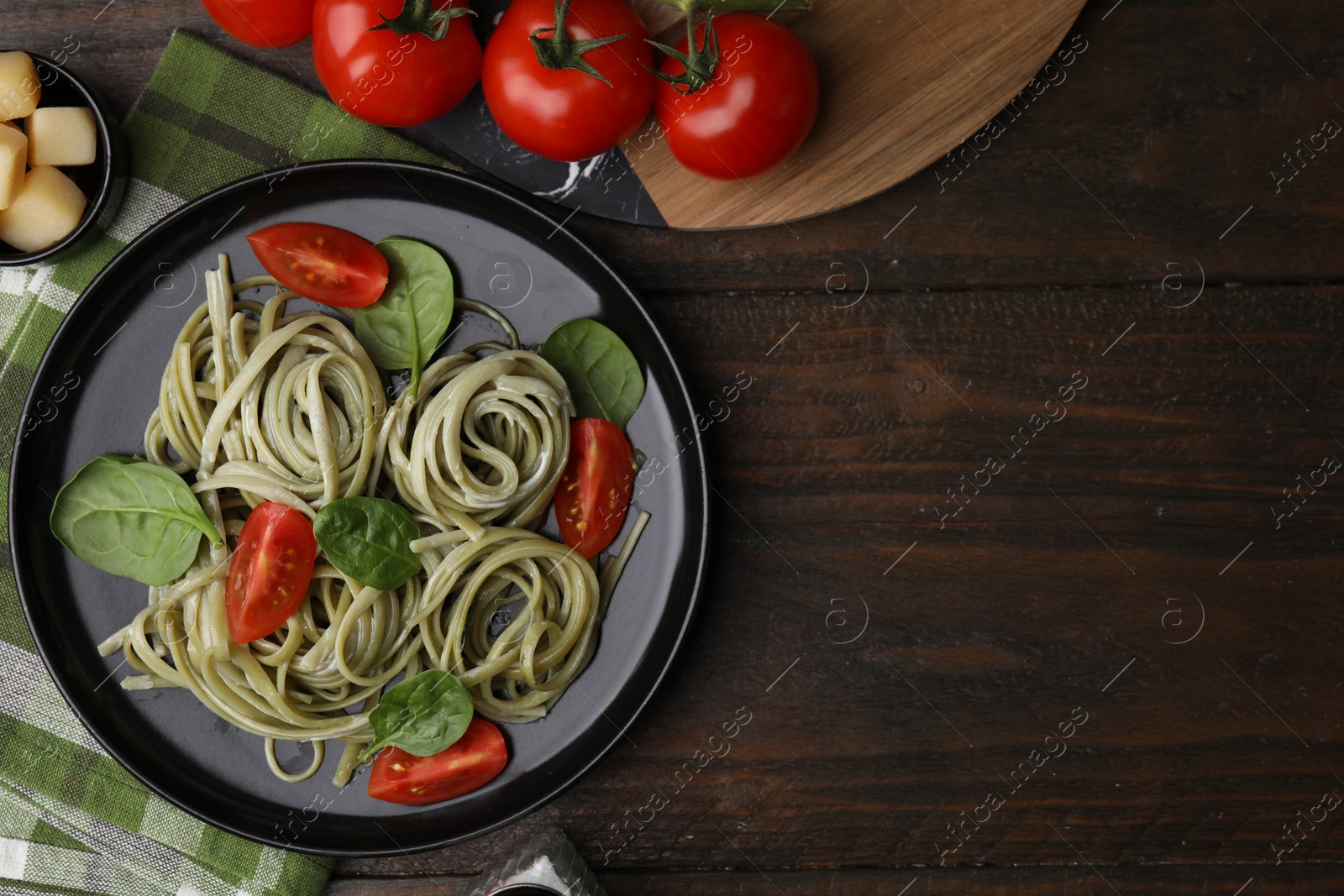 Photo of Tasty pasta with spinach, sauce and tomatoes on wooden table, flat lay. Space for text