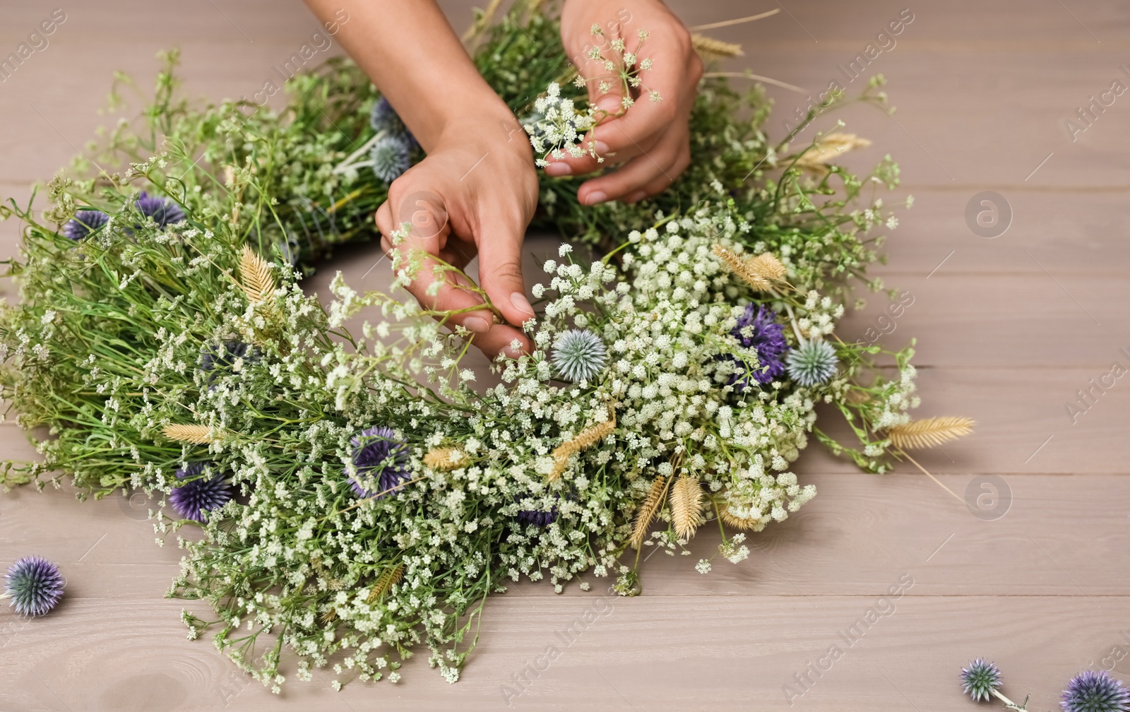 Photo of Woman making beautiful wreath of wildflowers at wooden table, closeup