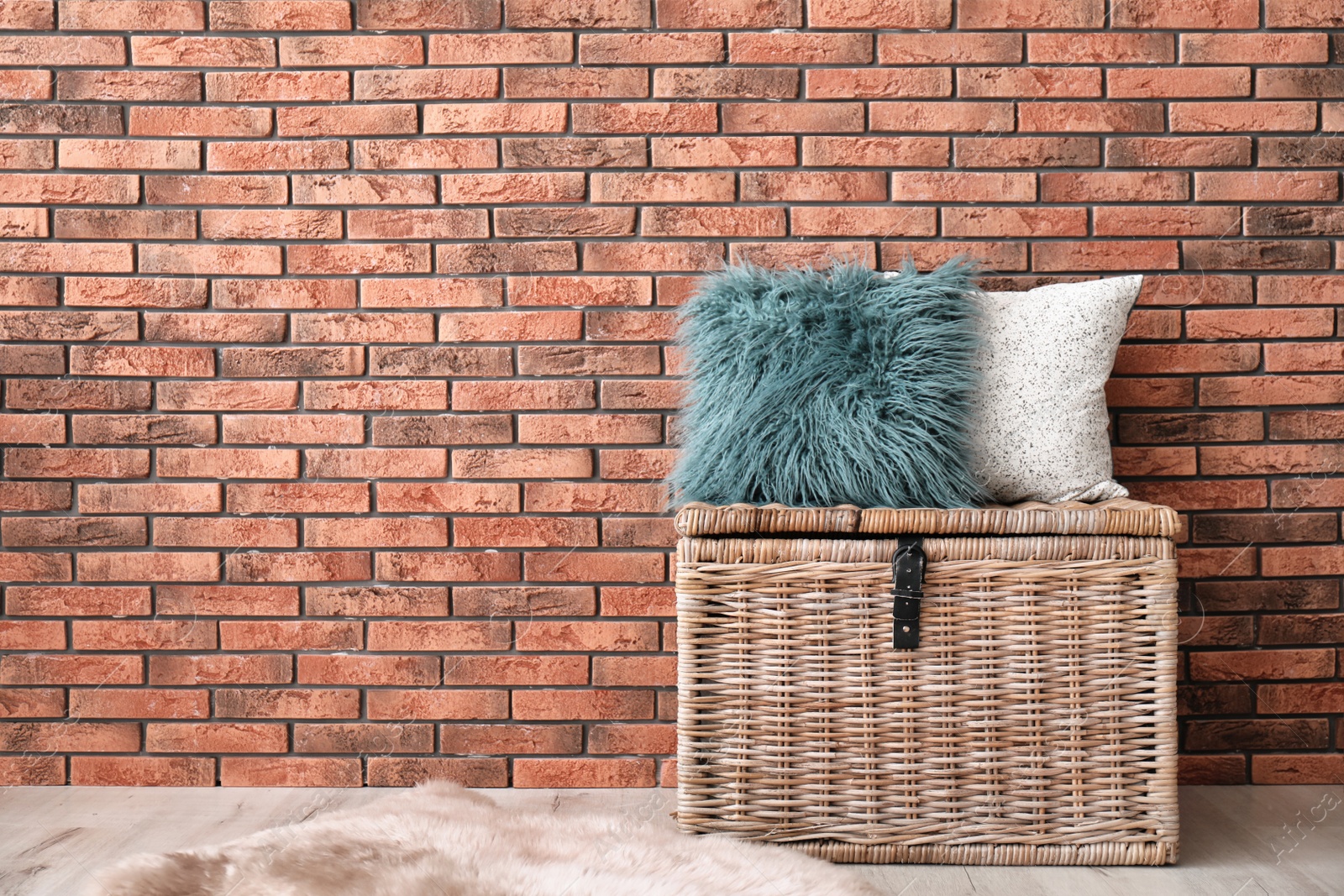 Photo of Soft pillows on wicker chest near brick wall