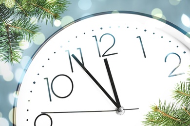 Clock showing five minutes till midnight with fir tree branches, closeup with bokeh effect. New Year countdown