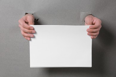 Photo of Man holding sheets of paper through holes in grey paper, closeup. Mockup for design