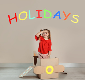 School holidays. Cute little child playing with cardboard plane near beige wall