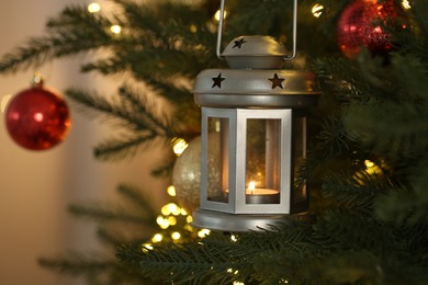 Photo of Christmas lantern with burning candle on fir tree against blurred background, closeup. Space for text