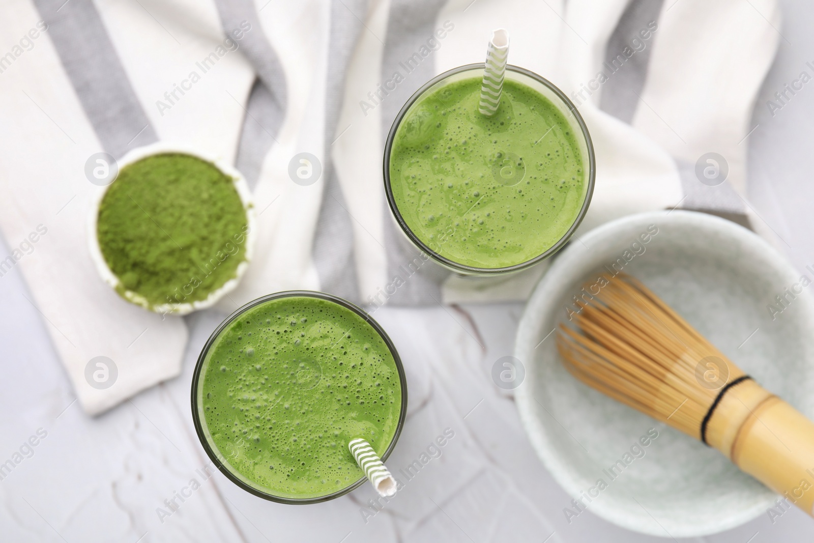 Photo of Glasses of tasty matcha smoothie on white textured table, flat lay