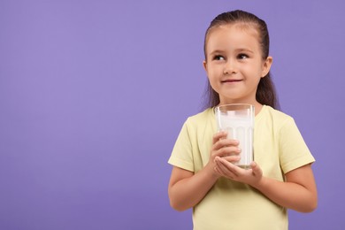 Photo of Cute girl with glass of fresh milk on violet background, space for text