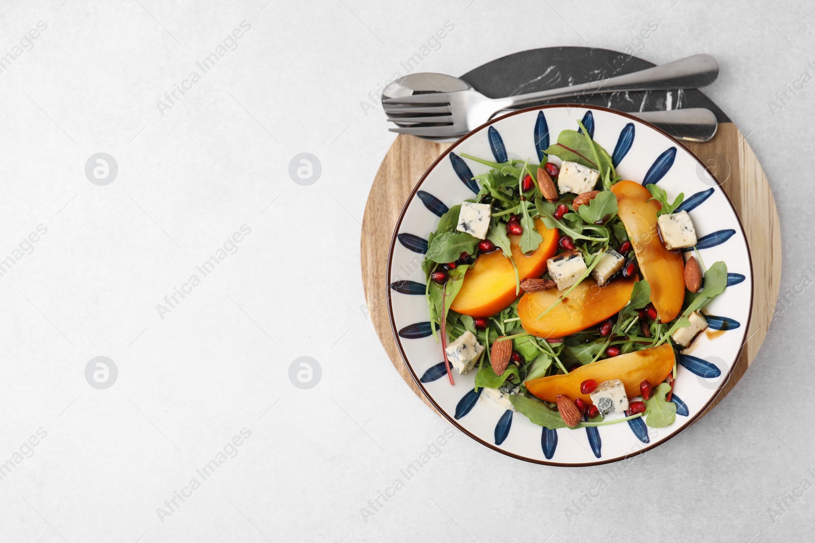 Photo of Tasty salad with persimmon, blue cheese, pomegranate and almonds served on white table, top view. Space for text