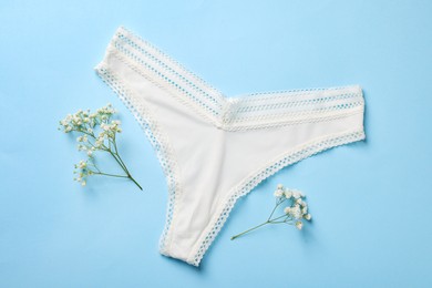 White women's underwear and flowers on light blue background, flat lay