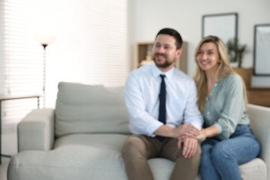 Photo of Blurred view of happy couple sitting on sofa at home, space for text