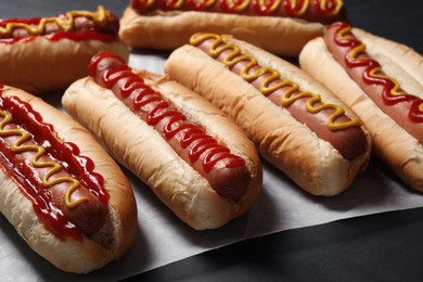 Fresh delicious hot dogs with sauces on black table, closeup