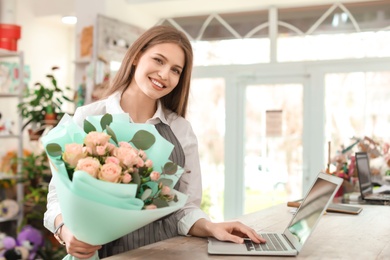 Photo of Female florist with bouquet and laptop working in flower shop