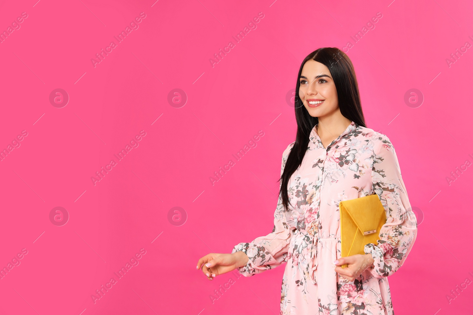 Photo of Young woman wearing floral print dress with elegant clutch on pink background. Space for text