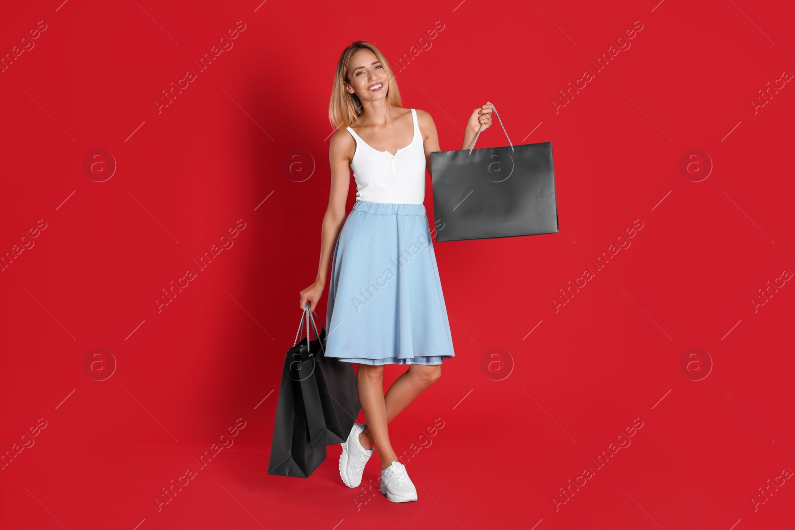 Photo of Happy young woman with shopping bags on red background. Black Friday Sale