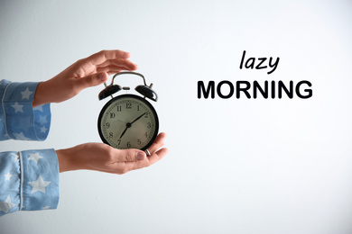 Image of Woman holding alarm clock on white background, closeup. Lazy morning