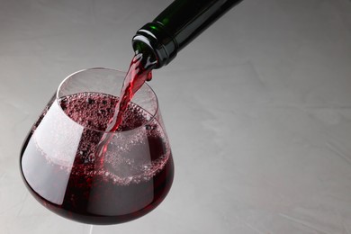 Photo of Pouring tasty red wine in glass at gray table, closeup. Space for text