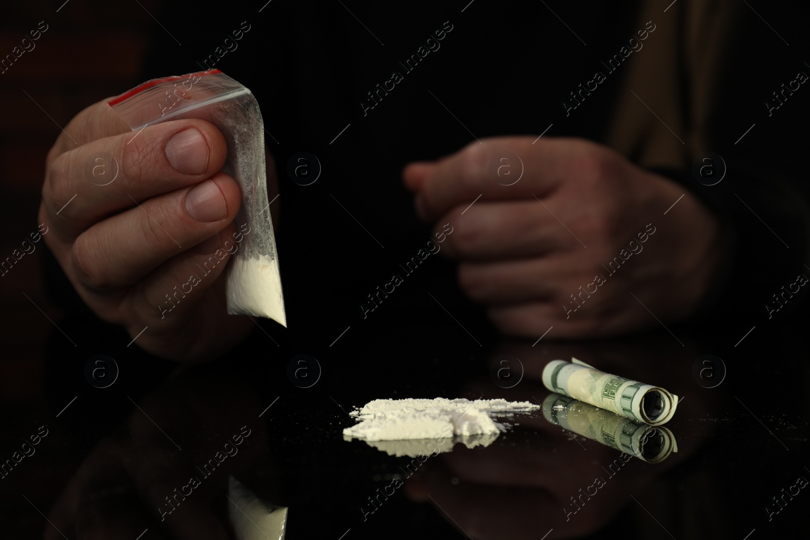 Photo of Drug addiction. Man with cocaine and rolled dollar banknote at black table, closeup