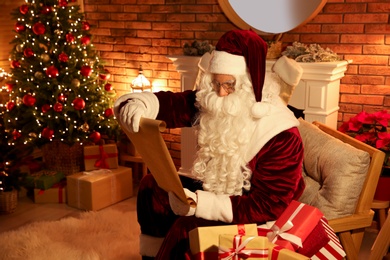 Photo of Santa Claus in armchair reading wish list indoors