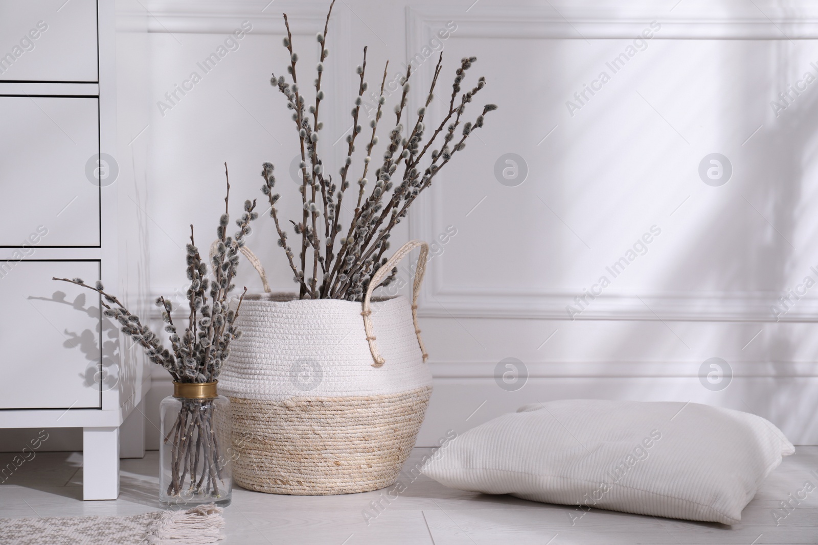 Photo of Pussy willow tree branches and pillow near chest of drawers in room