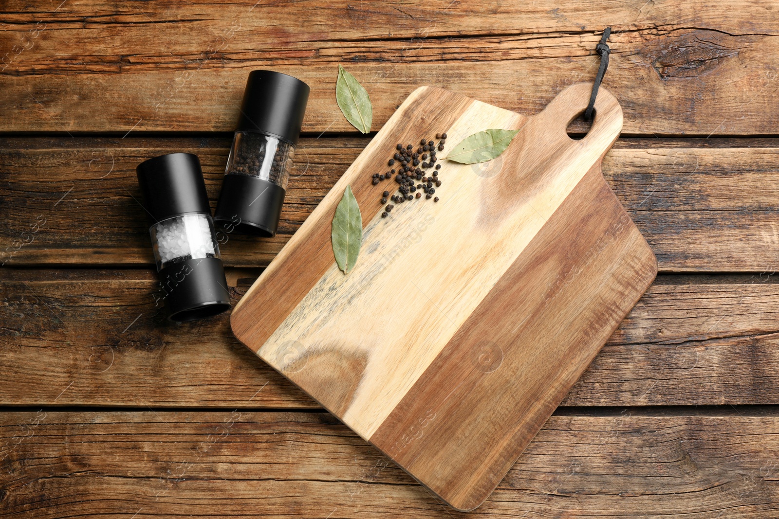 Photo of Cutting board and condiments on wooden table, flat lay. Cooking utensil