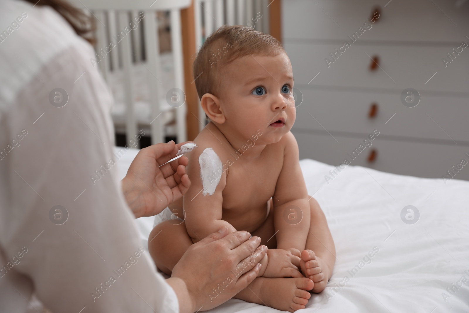 Photo of Mother applying moisturizing cream on her little baby at home, closeup