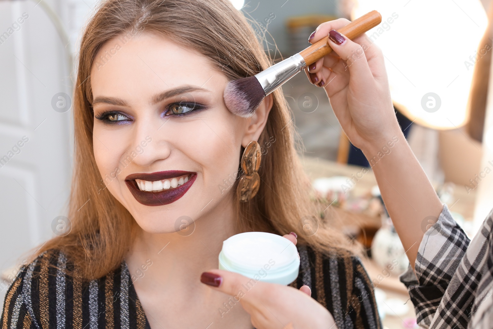 Photo of Professional makeup artist working with beautiful young woman in studio